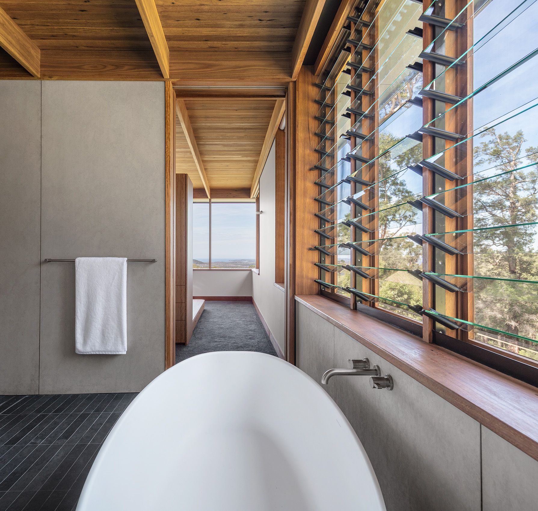 Freestanding bath beside a long louvred window
